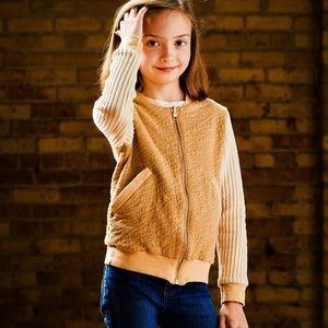 May include: A young person wearing a brown and cream zip-up jacket with long sleeves and blue jeans.