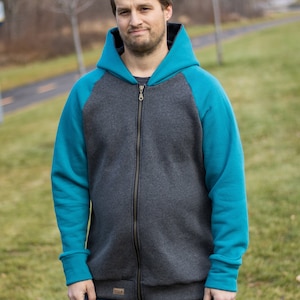 Op de afbeelding: Een grijs en turquoise hooded sweatshirt met een ritssluiting. De trui heeft een raglan mouw ontwerp.