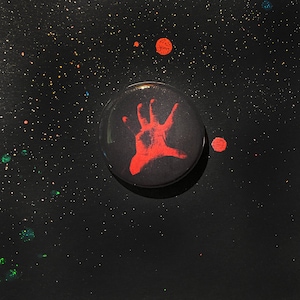 May include: A black button with a red handprint design on a black background with red dots.