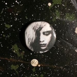 Puede incluir: Botón en blanco y negro con un retrato de cerca de una persona con el pelo largo.