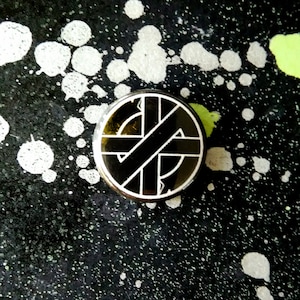 May include: A black and white pin with a circle design. The circle has a black background and a white design of a circle with a line through it.