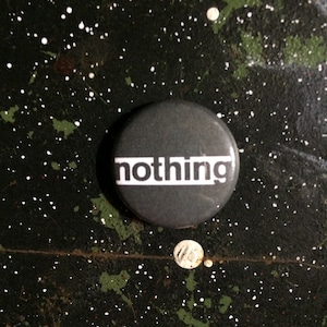 May include: A black button with the word "nothing" printed in white letters.