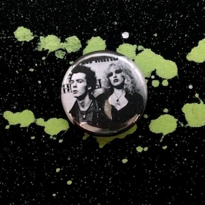 May include: A black and white button featuring a photo of two people with mohawks. The text "Hell" is visible in the background.