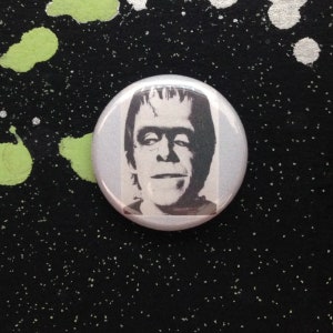 Peut inclure: Un bouton noir et blanc représentant un portrait rapproché de la créature de Frankenstein.