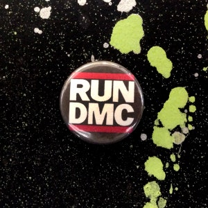 May include: A black and red button with the text "RUN DMC" in white letters.