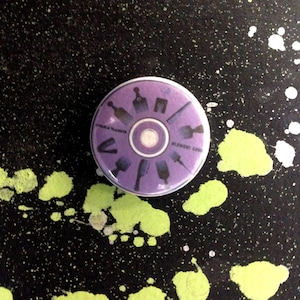 May include: Purple round button with a white center and a design of various tools around the edge. The text "SMALL BLADES" and "BLADE CUTS" are printed on the button.