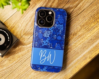 May include: A blue phone case with a floral pattern and the initials "BW" in white script. The case features a dark blue background with lighter blue and white floral accents. The case is on a wooden surface.