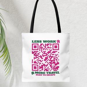 Op de afbeelding: Witte tote bag met zwarte handvatten en een roze en groene QR-code. De tekst op de tas luidt "Minder werk * Meer reizen Scannen om te ontsnappen".