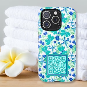 May include: A smartphone case with a floral pattern of teal dragonflies and blue flowers on a white background. The case has a QR code and a black camera module. The case is next to a white flower and a stack of white towels.