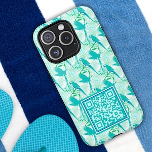 May include: A phone case with a vibrant tropical design featuring blue parrots, green leaves, and white flowers on a light green background. The case has a QR code in the lower right corner. The phone case is on a blue and white striped towel.