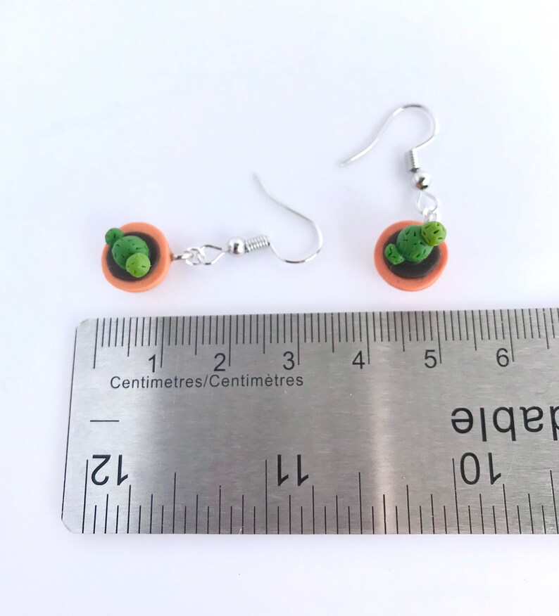 Puede incluir: Un par de pendientes de plata con un peque&ntilde;o tiesto de terracota y un amuleto de cactus verde. Los pendientes miden aproximadamente 3,2 cm de largo.