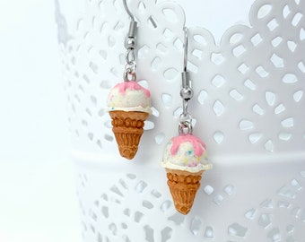 May include: A pair of silver dangle earrings featuring miniature ice cream cones with pink and white frosting and colourful sprinkles.