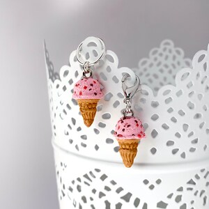 May include: Two pink and white ice cream cone charms with silver clasps. The ice cream cones are made of polymer clay and have a speckled appearance.