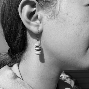 May include: A close-up of a person's ear with a silver earring featuring four stacked, round, white and brown ceramic beads.