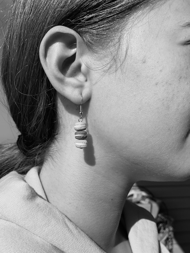 May include: A close-up of a person's ear with a silver earring featuring four stacked, round, white and brown ceramic beads.