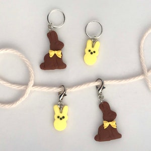 May include: Four handmade Easter bunny stitch markers. Two are brown with yellow bows and two are yellow with black eyes. The stitch markers are attached to a white string.