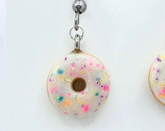 May include: A pair of donut earrings with white icing and colourful sprinkles. The earrings are made of polymer clay and have silver hooks.