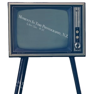 Puede incluir: Un televisor vintage negro y plateado con una pantalla azul oscuro. El televisor está sobre un juego de patas negras y tiene el texto "MOMENTS IN TIME PHOTOGRAPHY, N.Z. by Marie-Claire © 2017" en la pantalla. El televisor es de la marca SHARP.