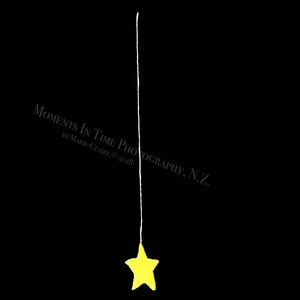 May include: A yellow star hanging from a white string against a black background. The text "Moments in Time Photography, N.Z. by Marie-Claire © 2018" is in the bottom left corner.