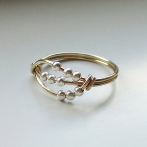 May include: A gold ring with a delicate design featuring a series of small silver beads woven into the band.