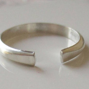 May include: A silver ring with a gap in the band. The ring is smooth and polished.