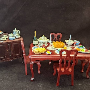 Könnte beinhalten: Ein Miniatur-Esszimmer-Set mit einem Mahagonitisch und Stühlen, einem Beistelltisch mit einem gläsernen Kuchenständer und einer Auswahl an Miniaturgeschirr und Lebensmitteln.