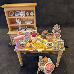 Pode incluir: Cena de cozinha em miniatura com um armário de madeira, mesa e vários utensílios de panificação. Inclui uma batedeira rosa, bolos, torta e chocolate Hershey's. A cena é definida em uma superfície escura.