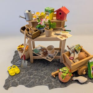 May include: Miniature garden scene with a wooden potting table, birdhouse, and various gardening tools. Includes a watering can, pots, and a wheelbarrow filled with supplies. A pair of yellow sandals and a small shovel are also present.