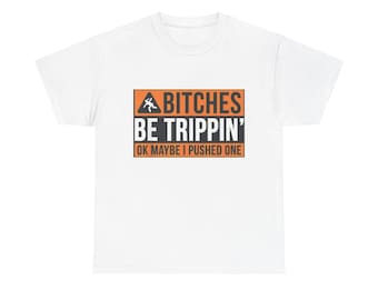 May include: White t-shirt with the text "BITCHES BE TRIPPIN'" in a black font, with an orange rectangle border. The text "OK MAYBE I PUSHED ONE" is below the main text. The shirt has a crew neck and short sleeves.