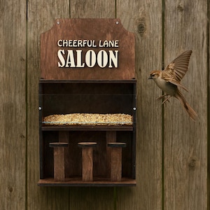 Könnte beinhalten: Ein hölzernes Vogelhaus mit dem Text "Cheerful Lane Saloon" an einem Holzzaun befestigt. Der Futterautomat hat ein rechteckiges Design mit einem Futtertablett und drei Sitzstangen. Ein kleiner brauner Vogel fliegt in der Nähe des Futterautomaten.