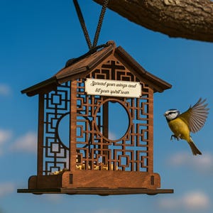 Peut inclure: Un nichoir en bois marron avec un motif géométrique décoratif est suspendu à une branche d'arbre. Le nichoir porte une pancarte avec le texte "Spread your wings and let your spirit soar". Un petit oiseau jaune et bleu vole à proximité.