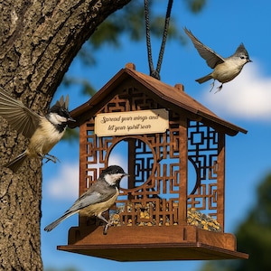 Op de afbeelding: Een bruin houten vogelhuisje met een dak in pagodestijl en ingewikkelde uitgesneden patronen. Het vogelhuisje hangt aan een tak. Een klein bordje leest "Spread your wings and let your spirit soar." Verschillende vogels zijn te zien.