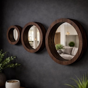 Può includere: Tre specchi rotondi con cornici in legno scuro di diverse dimensioni sono montati su una parete grigio scuro. Gli specchi riflettono l'interno di una stanza. Le cornici in legno hanno una finitura marrone scuro. Set di arte murale decorativo.