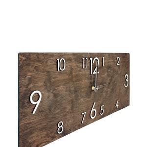 K&ouml;nnte beinhalten: Eine dunkelbraune Holzuhr mit wei&szlig;en Zahlen. Die Uhr ist nach rechts geneigt, und die Zeiger zeigen auf die 12 und die 4.