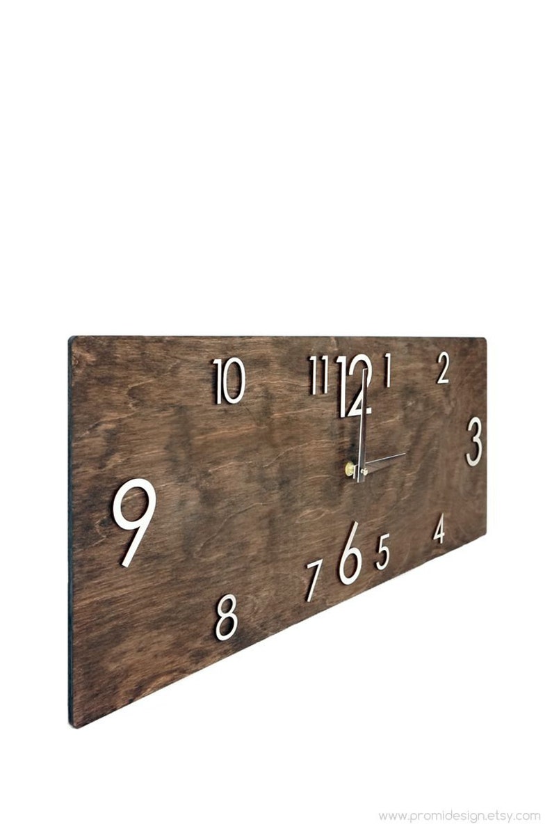 K&ouml;nnte beinhalten: Eine dunkelbraune Holzuhr mit wei&szlig;en Zahlen. Die Uhr ist nach rechts geneigt, und die Zeiger zeigen auf die 12 und die 4.