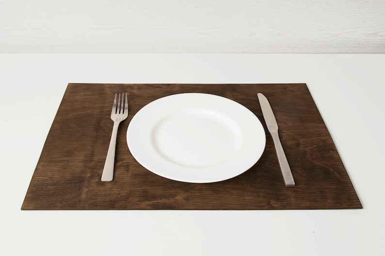 May include: A white ceramic dinner plate with a silver fork and knife on a dark brown wooden placemat.