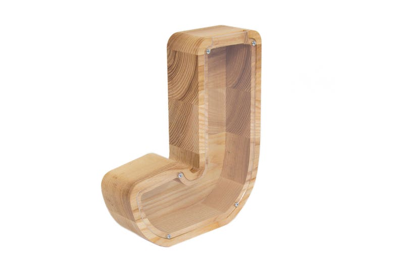 Pu&ograve; includere: Salvadanaio di legno a forma della lettera J. Il salvadanaio &egrave; realizzato in legno naturale con un fronte in plastica trasparente per vedere le monete all'interno.