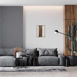 May include: A gray sofa with two throw pillows and a black throw blanket sits in a living room with a wooden wall and a clock on the wall. The clock has a white face with black numbers and a brown wooden frame.