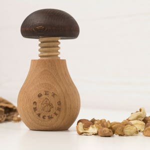 May include: A wooden nutcracker shaped like a mushroom with a brown top and a light brown base. The base has the words "Get Crackin'" engraved on it. There are some cracked walnuts in the foreground.
