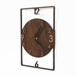 May include: A brown wooden clock with a square frame and a round face. The clock has gold numbers and hands.
