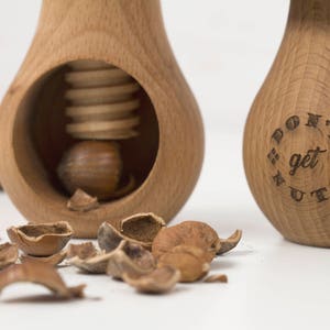 May include: Two wooden nutcrackers shaped like pears. One nutcracker has a screw mechanism and a hazelnut inside. The other nutcracker has the words "Don't get nuts" engraved on the side.