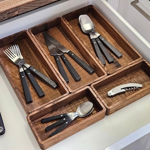 Può includere: Organizzatore per cassetti in legno con varie posate. Le posate includono forchette, coltelli, cucchiai e un cavatappi. Le posate hanno manici neri e lame argentate. L'organizzatore è in legno con finitura naturale.
