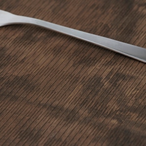 May include: A silver fork on a brown wooden surface with a wood grain pattern.