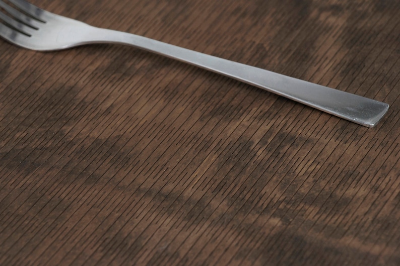 May include: A silver fork on a brown wooden surface with a wood grain pattern.