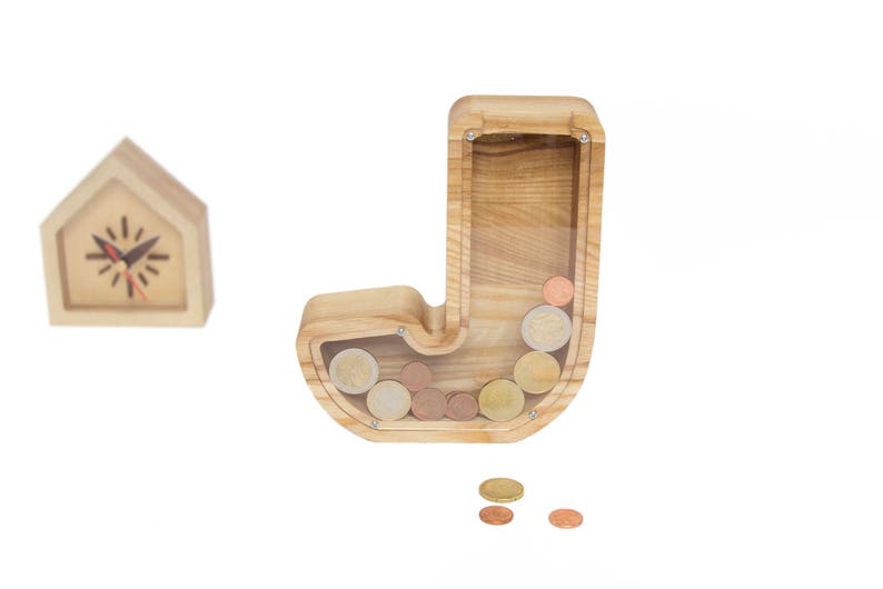 Pu&ograve; includere: Salvadanaio di legno a forma della lettera J. Il salvadanaio ha un fronte in plastica trasparente per vedere le monete all'interno. Il salvadanaio &egrave; pieno di monete.
