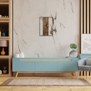 May include: A light blue media console with a wooden top and three drawers. A square wooden clock with black hands and Roman numerals is hanging on a white marble wall behind the console.