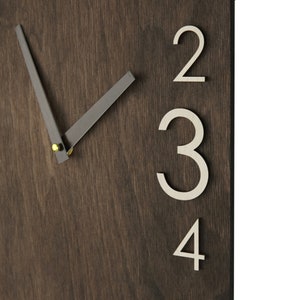 May include: A dark brown wooden clock face with white numbers 2, 3, and 4. The clock hands are black and point to the 10 o'clock position.