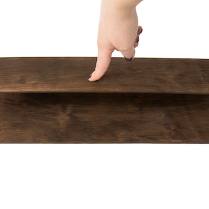 May include: Two pieces of dark brown wood veneer are stacked on top of each other. A hand is pressing down on the top piece of veneer.