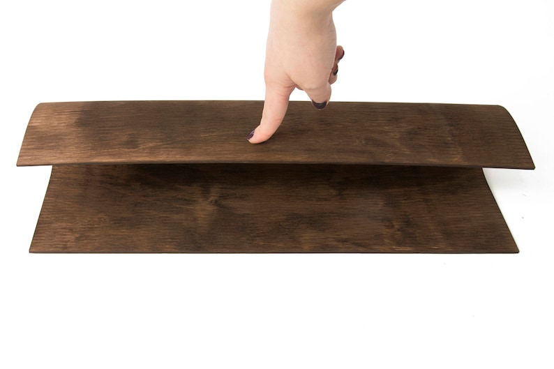 May include: Two pieces of dark brown wood veneer are stacked on top of each other. A hand is pressing down on the top piece of veneer.