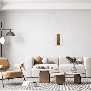May include: A white and brown rectangular clock with Roman numerals hangs on a white wall above a white couch with two beige pillows. The couch is in a living room with a beige armchair, two wooden coffee tables, and a vase with dried grass.